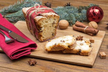 Fototapeta na wymiar Christmas cake with raisins and cinnamon sticks on board. Fork with knife on red napkin. Fir branches on table