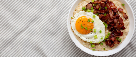 Homemade Cheesy Bacon Savory Oatmeal Bowl on cloth, view from above. Top view, overhead, flat lay. Copy space.