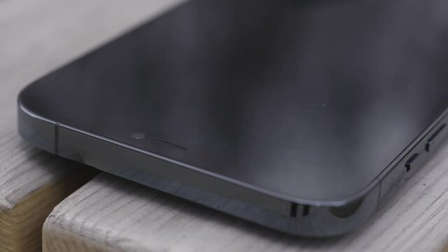 Close up of a part of a black screen of a new smartphone on wooden bench background. Action. New turned off device is left on a bench.