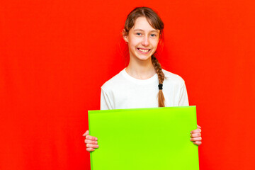 Front view teenager girl showing blank paper.Mock up,banner,copy space.Bright red studio wall.