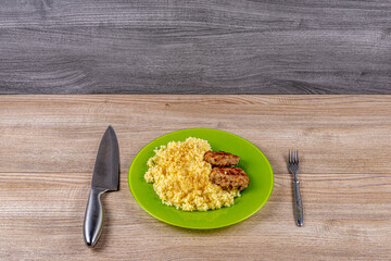 Millet porridge with minced pork cutlets on a plate on the table with a fork and a knife