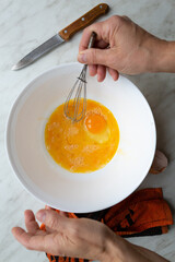 female hands whip omelet in bowl of raw eggs on the kitchen table by the window, top view