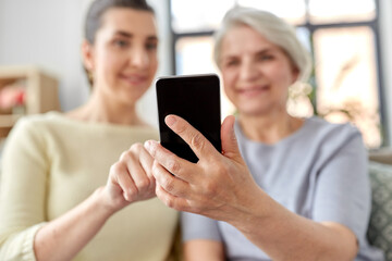 family, generation and technology concept - happy smiling senior mother and adult daughter with smartphone at home