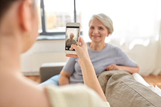 family, generation and people concept - adult daughter with smartphone photographing happy smiling senior mother at home