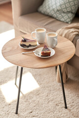 food, junk-food, culinary, baking and holidays concept - pieces of delicious cake on saucers with spoons and coffee cups on wooden table