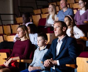 mother, father and their children sitting at perfomance in theatrical auditorium