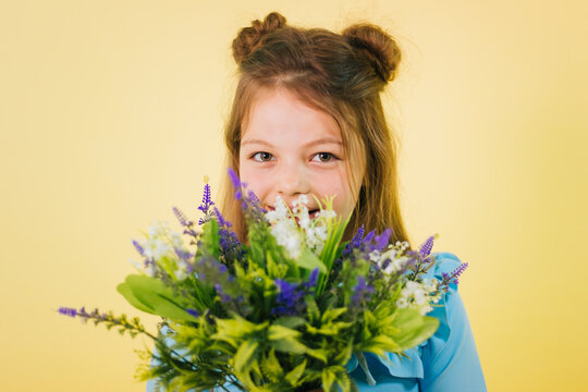 A girl of twelve years old in a blue dress on a yellow background holds lavender and lily of the valley flowers in her hands. Fashionable child. Studio photo