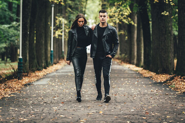 Obraz premium Dramatic shot of couple in love both weard in black leather jackets, holding hands and strolling in autumn park.