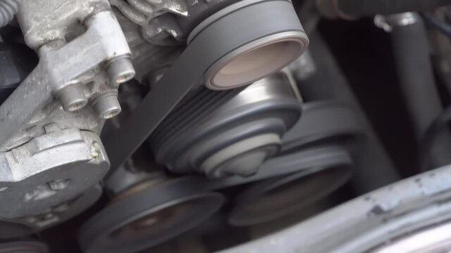 The car engine is running. Close-up rotation of parts, belt, generator and pulleys on the car engine.