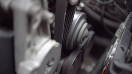 The car engine is running. Close-up rotation of parts, belt, generator and pulleys on the car engine.