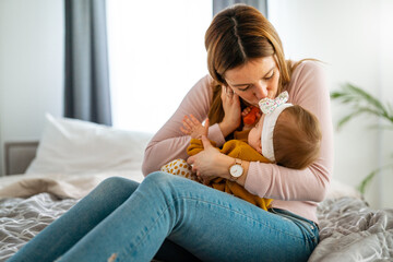 Mother and baby daughter plays, hugging, kissing at home. Happy family.