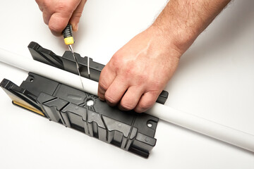 A man cuts a polystyrene baseboard with a clerical knife using a box to cut corners. Renovation...