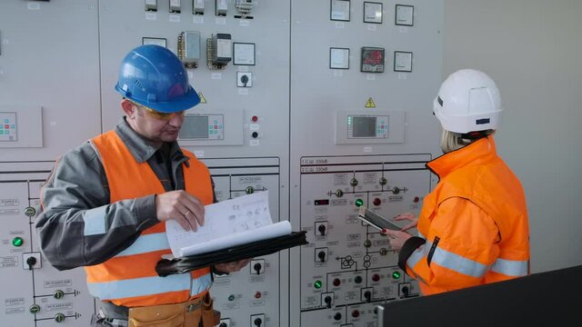 Engineer with papers shows female inspector with tablet installed new equipment at contemporary wind power plant substation