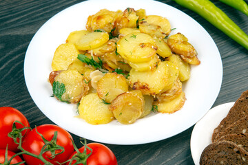 cooked fried potatoes with herbs and vegetables in a white plate on a wooden table