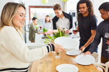 Woman laying table for lunch in kitchen with friends