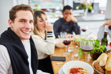 Happy friends eating pasta together at table in kitchen