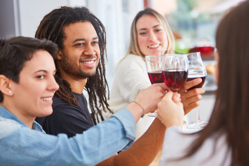 Happy friends at home in shared flat toast with glass of red wine