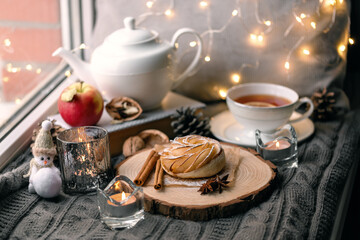 A cup of hot tea with lemon in an early winter morning by the window. Knitted wool warm blanket, hot homemade apple cakes with cinnamon and star anise . Decor. Home winter holiday concept.