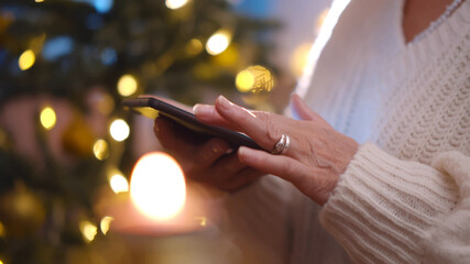 Close up of senior woman surfing internet on tablet pc near christmas tree