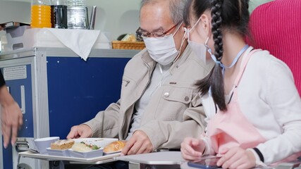 Asian grandfather is teaching to wear correctly the facial mask to his granddaughter.Coronavirus prevention on the airplane.travel concept