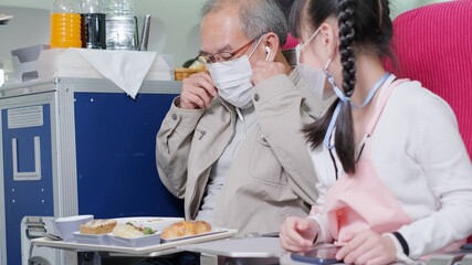 Asian grandfather is teaching to wear correctly the facial mask to his granddaughter.Coronavirus prevention on the airplane.travel concept