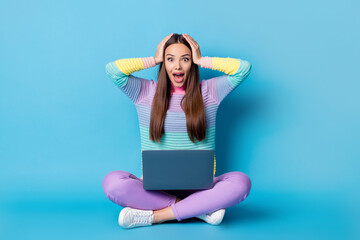 Portrait of glad cheerful amazed girl sitting lotus position crossed legs using laptop great news isolated on bright blue color background