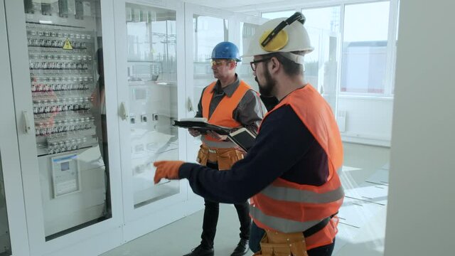 Bearded engineer shows new cases with equipment to skilled inspectors checking electrical substation premises before start