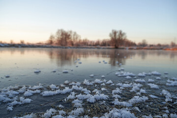 Fototapeta premium Breath of winter, first ice on the lake, dawn on a frosty morning with frost on the grass, close-up of frost, patterns on the first ice.