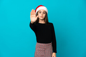 Little girl with Christmas hat isolated on blue background making stop gesture