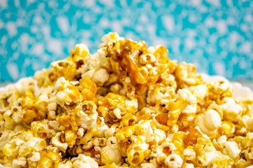 Closeup of a pile of caramel popcorn against a blue background.