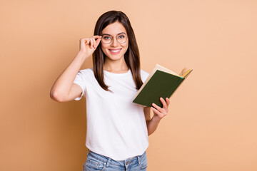 Photo portrait of girl wearing eyewear smiling reading book studying in college isolated pastel beige color background