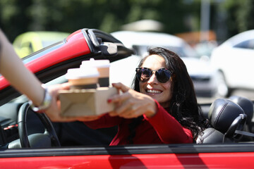 Box of coffee is handed over to smiling woman in car. Food and drink delivery concept