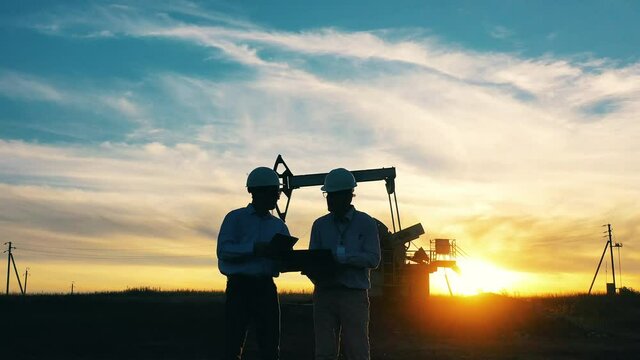 Oil industry workers talking in an oil field by an oil pump at sunset