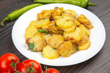cooked fried potatoes with herbs and vegetables in a white plate on a wooden table