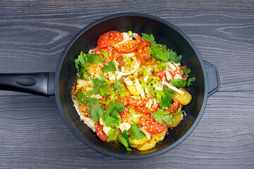 cooked fried potatoes with herbs, spices and vegetables in a black pan on a wooden table