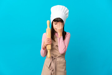 Little girl holding a rolling pin isolated on blue background with tired and sick expression