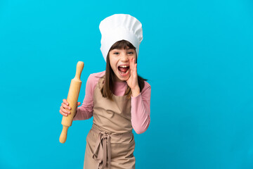 Little girl holding a rolling pin isolated on blue background shouting with mouth wide open