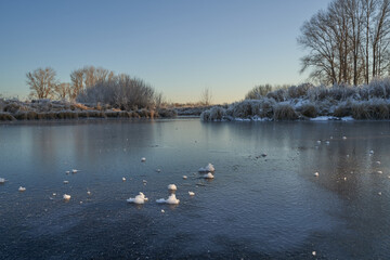 Naklejka premium Breath of winter, first ice on the lake, dawn on a frosty morning with frost on the grass, close-up of frost, patterns on the first ice.