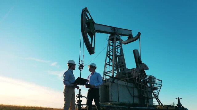 Two oil industry workers having a discussion in an oil field by an oil pump