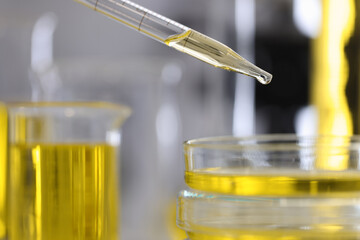 Yellow oil drips from a dispenser into test tube in laboratory. Research in scientific field concept