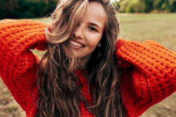Outdoor portrait of a smiling young woman wearing a knitted orange sweater posing on nature...