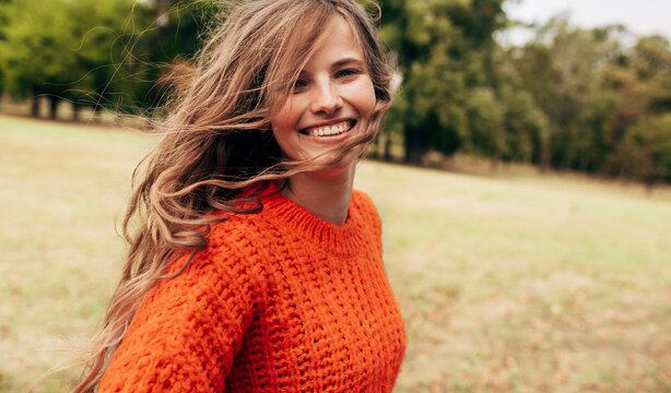 Positive young woman wearing a knitted orange sweater posing on nature background. A cheerful female has a joyful expression during walking in the park.