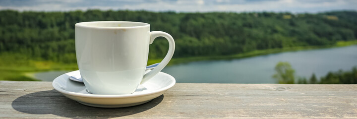 White cup of hot coffee on balcony with natural and mountains, hills background. Beverage, breakfast.
