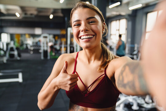 Smiling athletic sportswoman showing thumb up while taking selfie photo