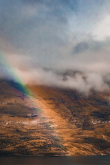 Rainbow coming out of the clouds in front of the mountains