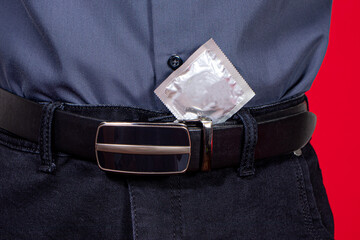 A man's torso and a condom in his pocket on a red background. Protected sex, safety from sexually...