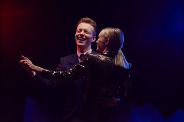 Waist up portrait of happy young couple dancing together while enjoying party at prom night against dark background, copy space