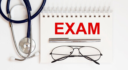 stethoscope,glasses and pen with notepad with text EXAM
