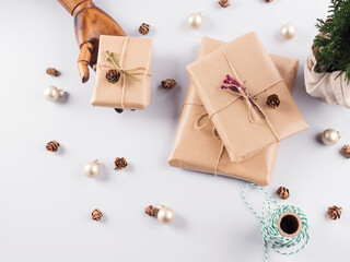 Fototapeta na wymiar Christmas gifts wrapped in craft paper, pine cones and minimal festive ornament in wooden hand. Flat lay