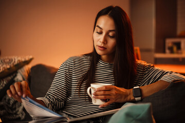 Thinking beautiful woman writing down notes while sitting on sofa